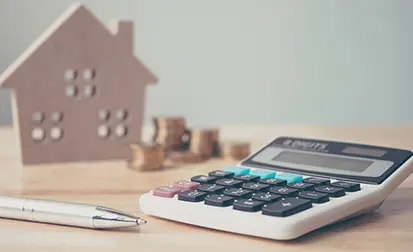 Calculator with wooden house and coins stack and pen on wood table